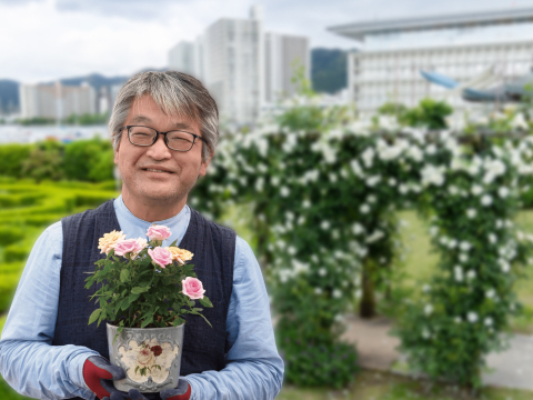 バラの鉢植えを持つ男性と背景のアーチ状のバラ園風景